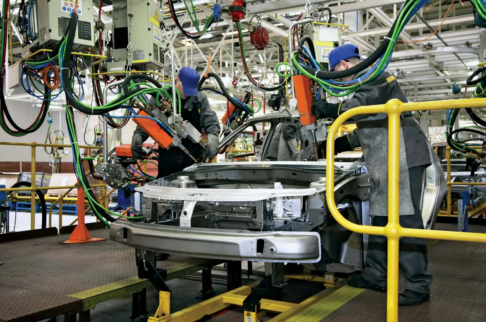 Workers assemble car parts on a modern factory production line, showcasing industrial manufacturing.